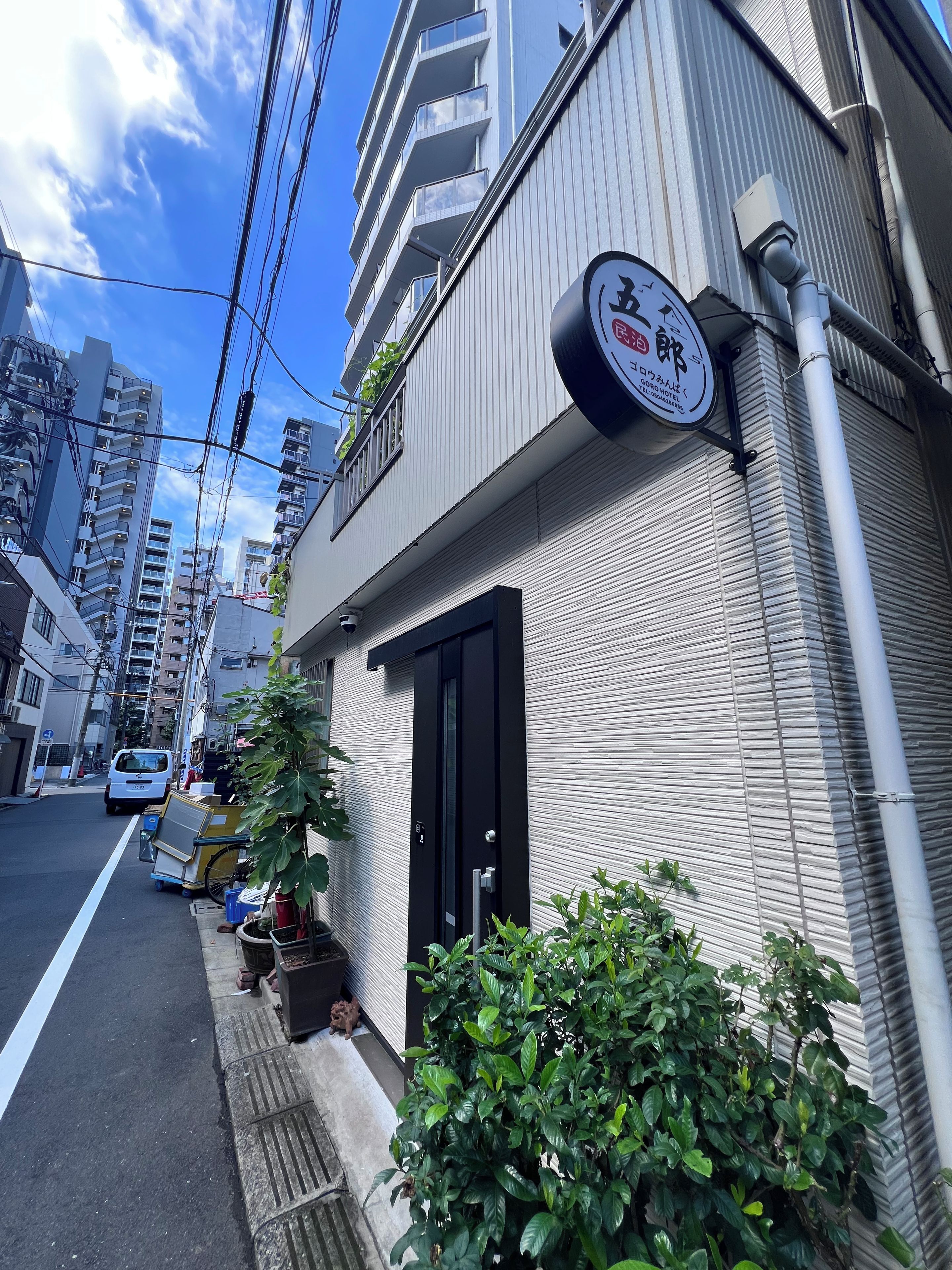 A building with a sign indicating a hotel, a black door, and a small garden area with plants.