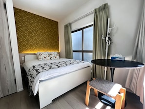Une chambre d’hôtel avec un lit, une table de chevet, une chaise, une fenêtre avec des rideaux et un mur orné d’un motif.