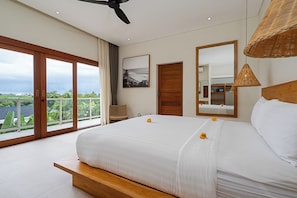 A bedroom with a large bed, a ceiling fan, a view through a sliding door, a wooden bench, and a wicker lamp. - High End Luxury 3BR Villa Walking Distance to Nuanu City (Tabanan)