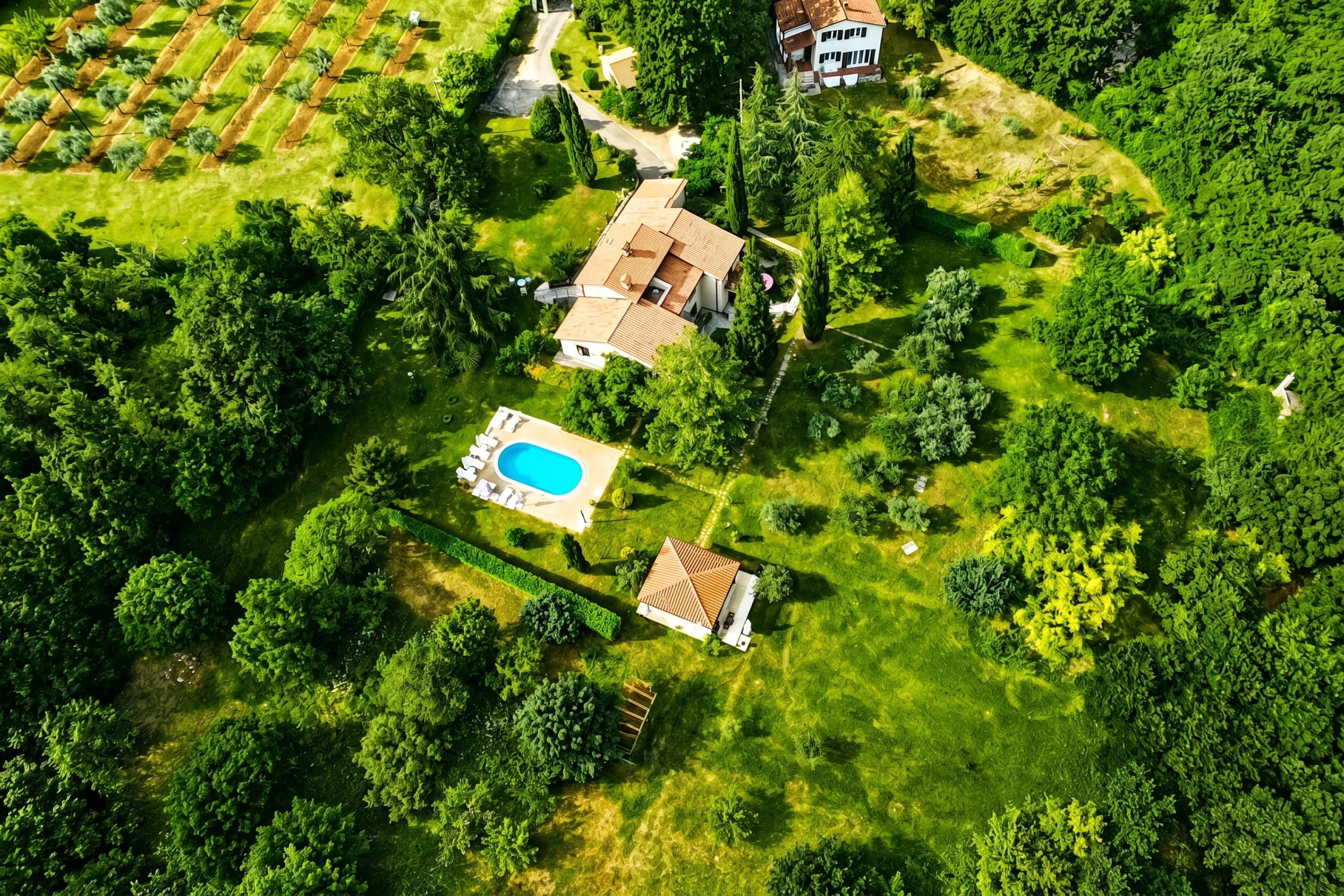 An aerial view of a property with a swimming pool, a house with a tiled roof, and surrounding greenery.