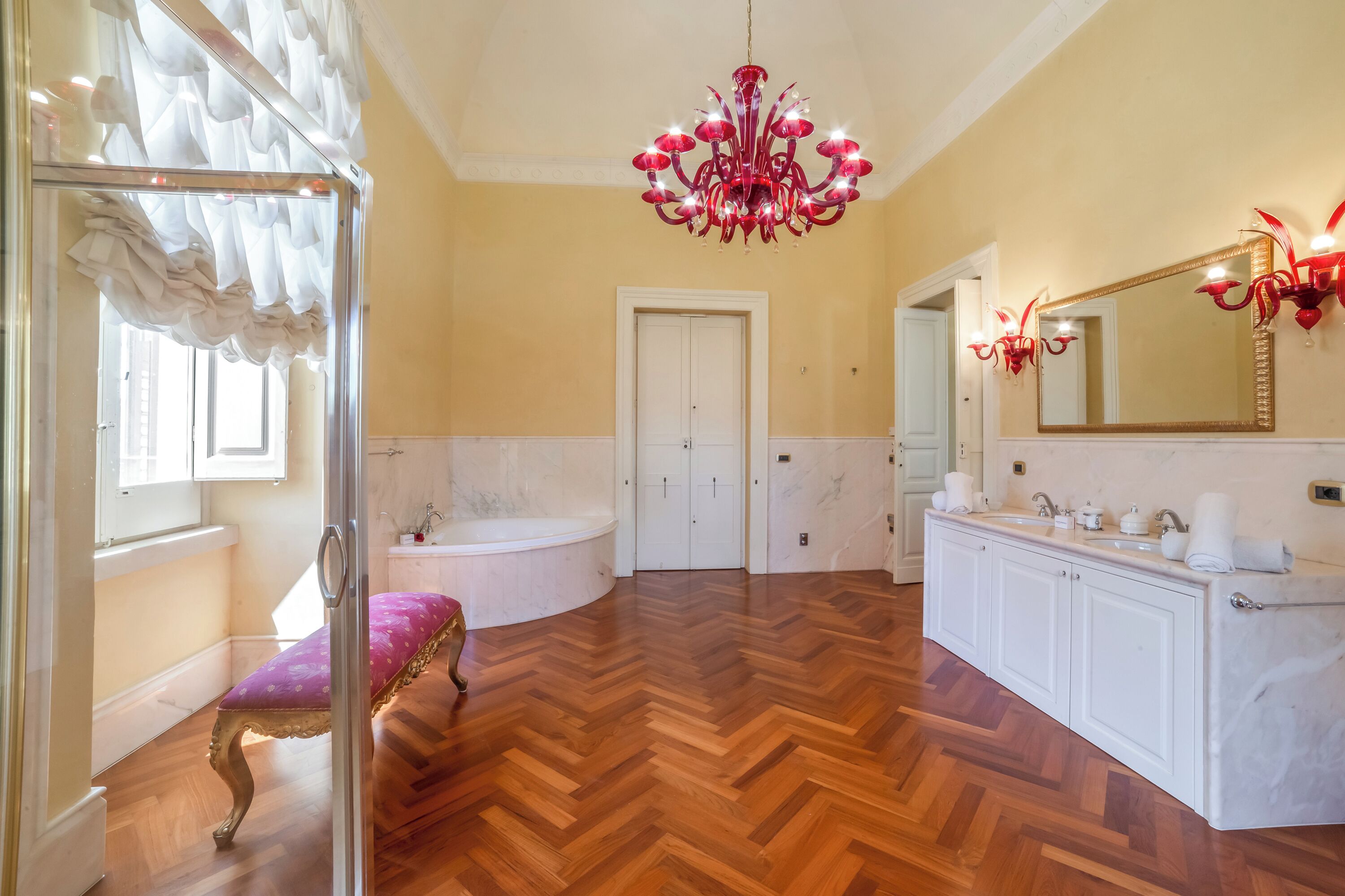A spacious bathroom with a wooden herringbone floor, a large mirror, a freestanding bathtub, and a vanity with a sink and towel rack.