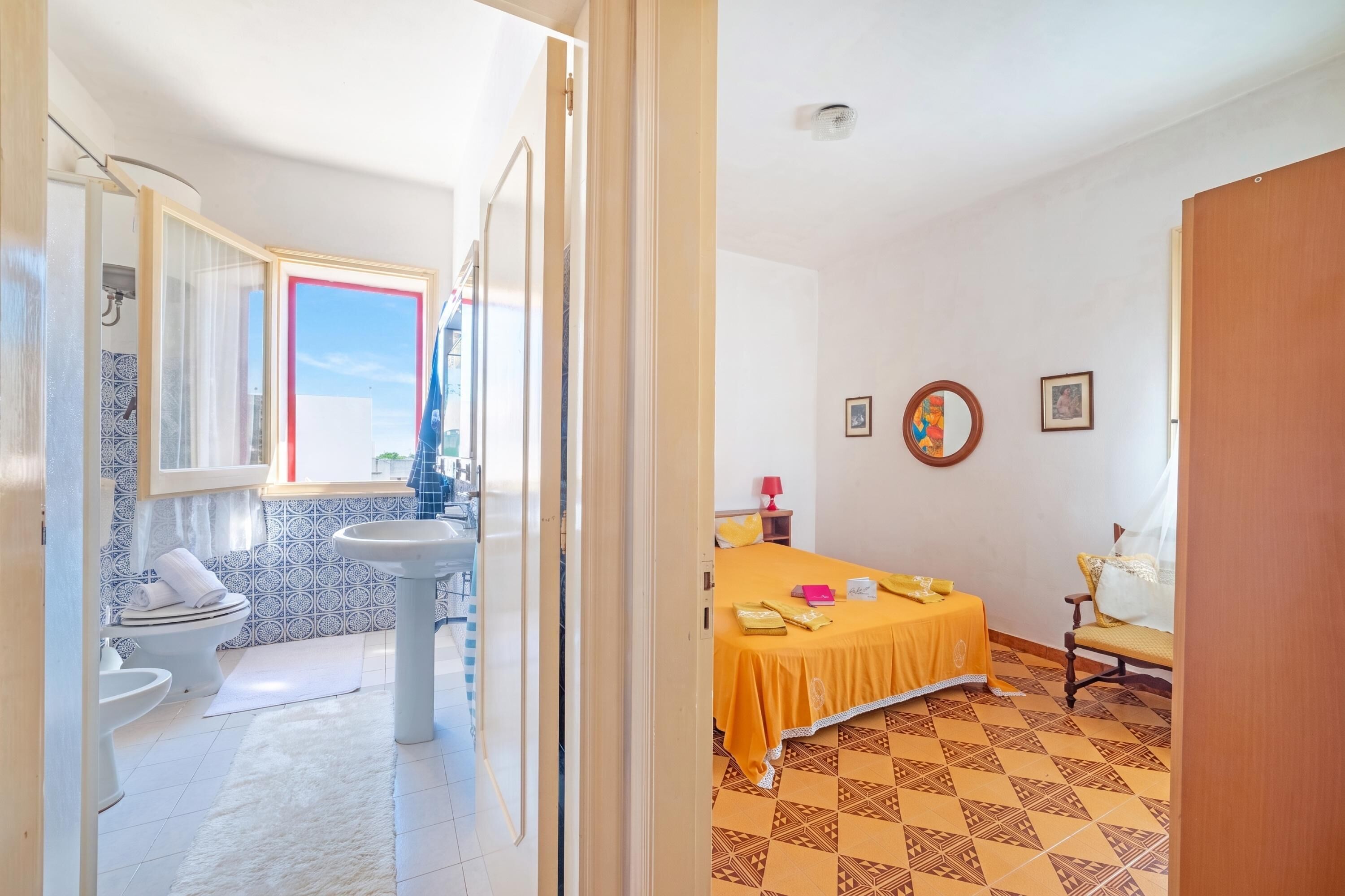 Una habitación de hotel con baño, una cama con cubrecama amarillo y una pequeña mesa con una silla.