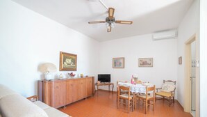 Uma sala de estar com sofá, mesa de jantar, cadeiras, televisão e ventilador de teto.