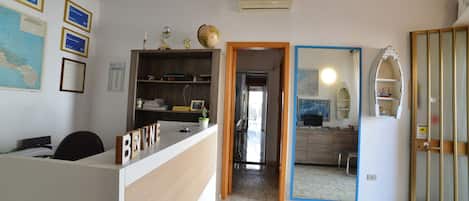 Una recepción con una placa de identificación, un ventilador de techo, un mapa en la pared y una puerta que da a una zona de cocina.