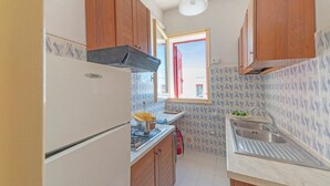 Uma cozinha compacta com armários de madeira, uma pia de aço inoxidável e uma janela com uma persiana vermelha.