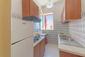 Eine kleine Küche mit Holzausstattung, einem Edelstahlspülbecken und einem Fenster mit rotem Rollo.