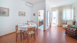 Uma sala de jantar com mesa posta para quatro, cozinha ao fundo, e área de estar com sofá e poltronas.