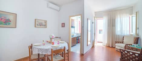 A dining area with a table set for four, a kitchen in the background, and a living area with a sofa and armchairs.