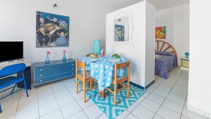 Ein Zimmer mit einem Bett, einem Schreibtisch mit Computer, einem Sessel, einem Tisch mit Tischdecke und Wandbildern.