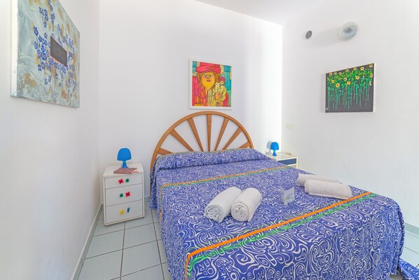 Ein Schlafzimmer mit einem hölzernen Bett, einem Nachttisch, zwei Wandbildern.