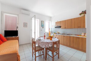 Ein Zimmer mit einem Bett, einem Esstisch mit Stühlen, einer Küchenzeile und einer Klimaanlage.