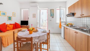 A compact kitchen with wooden cabinets, a dining table with chairs, and a TV in the background. - Leuca Relax & Sea n.1b, Castrignano del Capo, Italy (Castrignano del Capo)