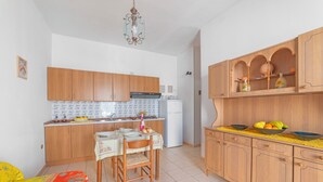 Une cuisine compacte avec des meubles en bois, une table à manger avec des chaises, un réfrigérateur et un luminaire suspendu.