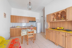 Eine kleine Küche mit Holzschränken, einem Esstisch mit Stühlen, einem Kühlschrank und einer Pendelleuchte.