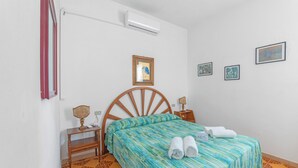 Une chambre à coucher avec un lit en bois, une table de chevet, un bureau, une chaise, un climatiseur fixé au mur et un sol à motifs.