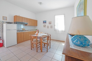 A kitchen with wooden cabinets, a white refrigerator, a dining table with chairs, and a window with blinds. - Leuca Relax & Sea n.4bbis, Castrignano del Capo, Italy (Castrignano del Capo)