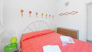 Une chambre à coucher avec un lit blanc, une chaise verte, une commode en bois et un mur décoré de motifs floraux.