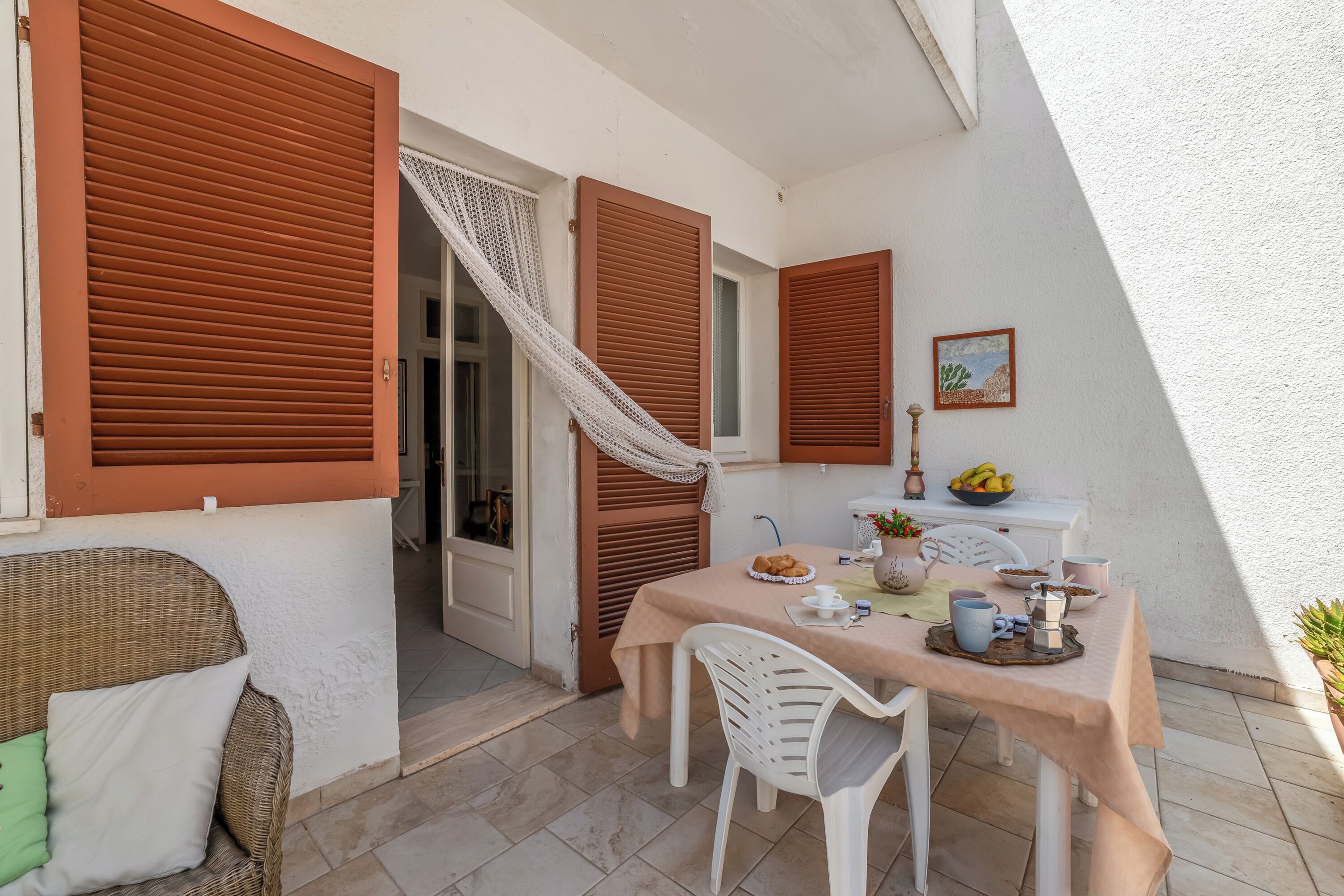 A dining area with a table set for two, a wicker chair, and a white chair.