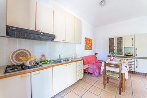 A kitchen with white cabinets, a stove, and a sink. There is a dining table with chairs and a vase of flowers. - Leuca Relax&Sea n.3bbis, Castrignano del Capo, Italy (Castrignano del Capo)