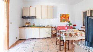 Una cucina compatta con fornello a gas, lavello e pensili. C'è un'area pranzo con tavolo e sedie, e una TV su un mobile.