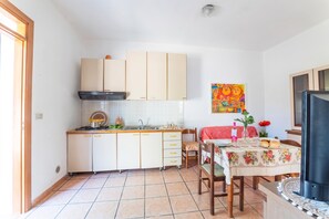 A compact kitchen with a gas stove, sink, and cabinets. There is a dining area with a table and chairs, and a TV on a stand. - Leuca Relax&Sea n.3bbis, Castrignano del Capo, Italy (Castrignano del Capo)