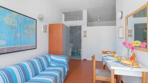 Ein Zimmer mit einem gestreiften Sofa, einem Esstisch mit einem Stuhl, einer Karte an der Wand und einer Badezimmertür.