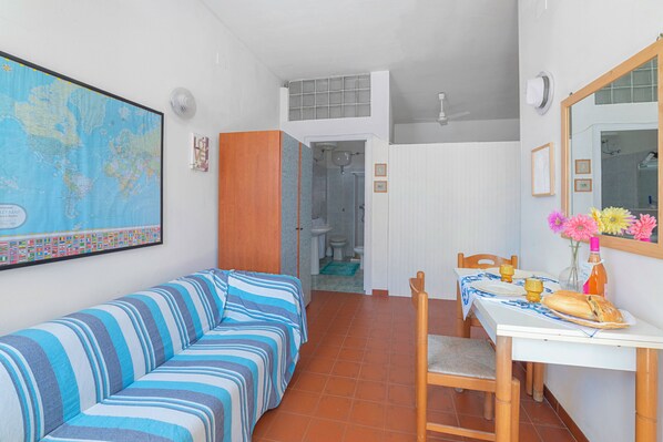 Ein Zimmer mit einem gestreiften Sofa, einem Esstisch mit einem Stuhl, einer Karte an der Wand und einer Badezimmertür.