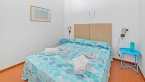 Ein Zimmer mit einem Bett, einem kleinen Tisch, einer Wandleuchte und einem gerahmten Bild.
