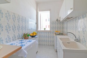 A narrow kitchen with white and blue patterned tiles, a window with a view, a sink, and a table with a fruit bowl. - Leuca Relax&Sea n.3b, Castrignano del Capo, Italy (Castrignano del Capo)