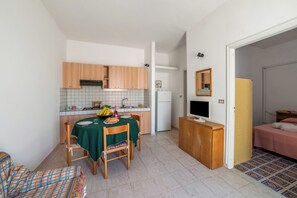 Eine kompakte Küche mit Holzausbau, einem Esstisch mit Stühlen, einem kleinen Kühlschrank und einem Fernseher auf einem Holzschrank.