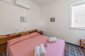 Ein Hotelzimmer mit Bett, Nachttisch aus Holz, Fenster und Wandklimaanlage.
