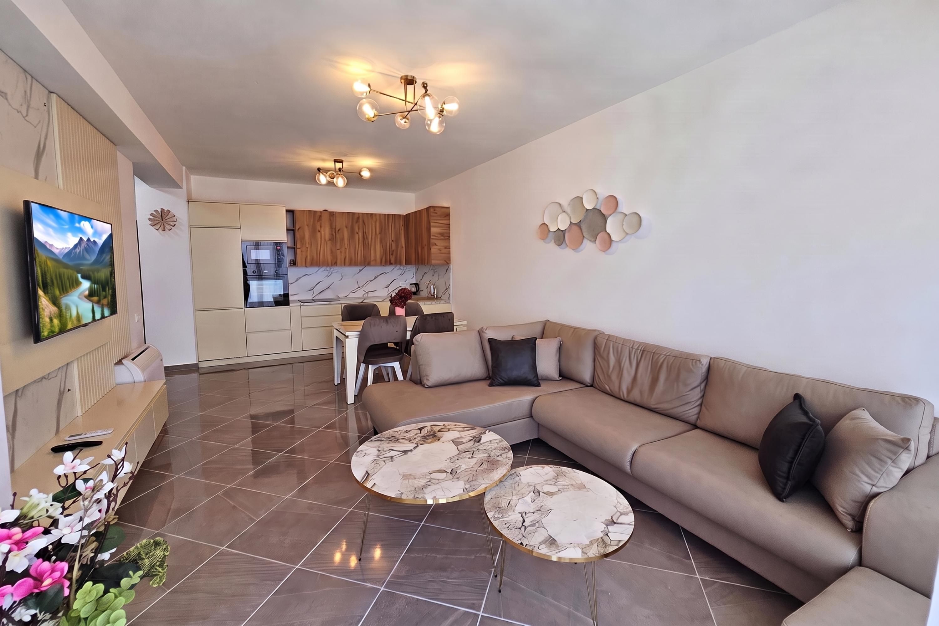 Un soggiorno moderno con un divano, due tavolini rotondi, una TV e una cucina sullo sfondo.