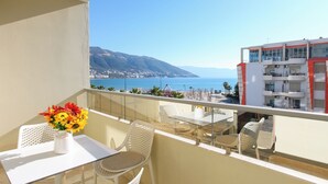 A balcony with a table and chairs, a vase of flowers, and a view of the sea and mountains. - Ellin Apartment, Vlore, Albania (Vlore)