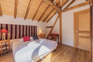 Ein Schlafzimmer mit Holzboden, einem Bett mit weißen Leinen, einem roten Kopfkissen, einem gestreiften Vorhang und einer Holztür.