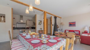 A dining area with a table set for four, a kitchen in the background, and a red sofa in the living area. - Chalet Les Airelles Mont-Blanc View, Chamonix, France (Chamonix)