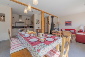 Ein Essbereich mit Tisch für vier Personen, eine Küche im Hintergrund und ein rotes Sofa im Wohnbereich.