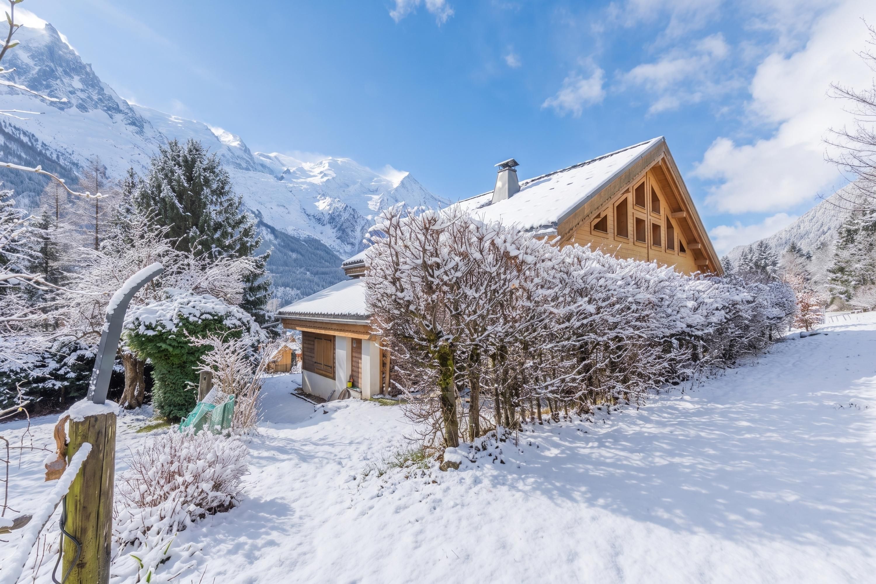 Un chalet en bois, doté d’un toit en pente, entouré d’arbres couverts de neige et avec des montagnes en arrière-plan.