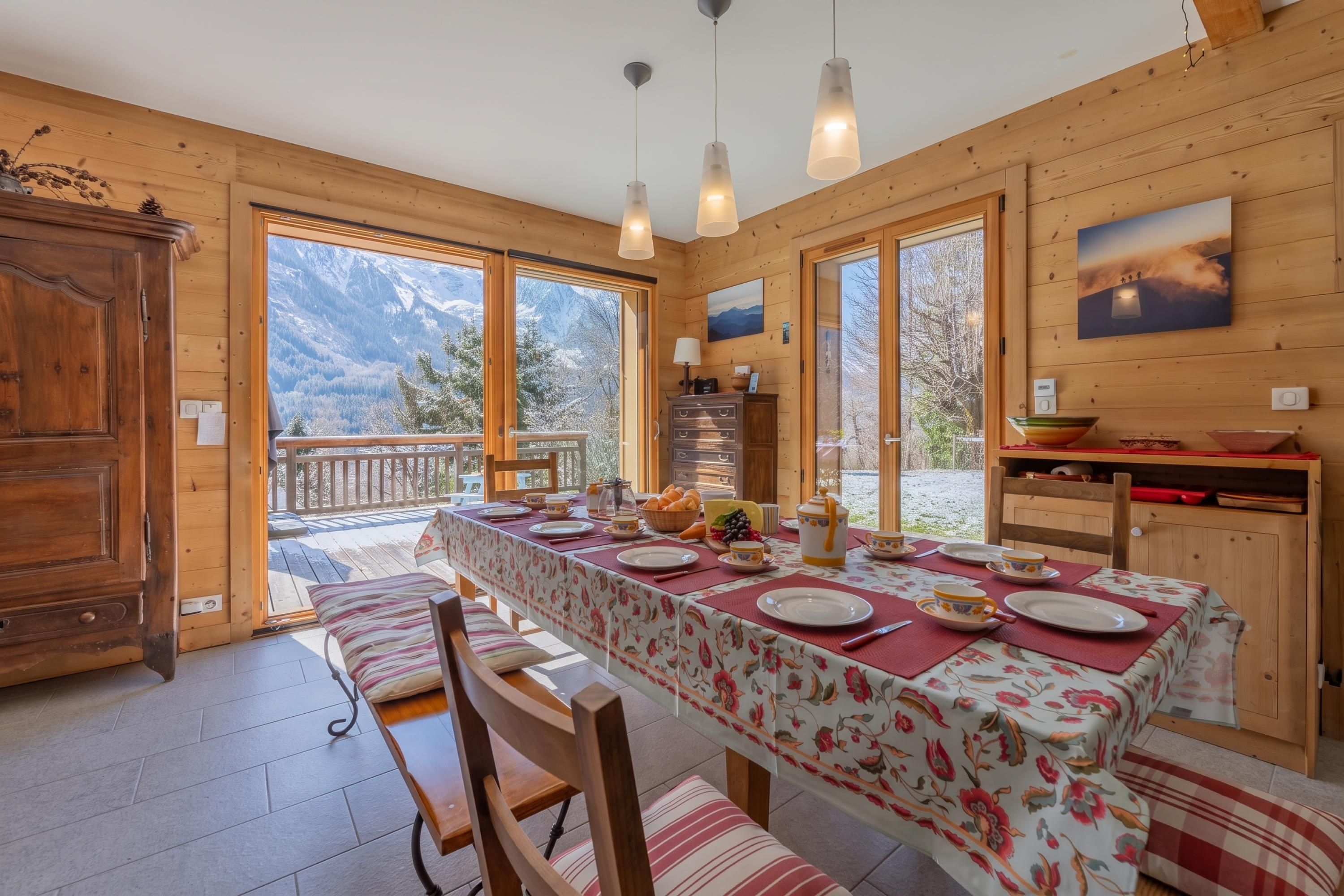 Un intérieur en bois avec une table à manger pour quatre personnes, un buffet en bois et une vue sur les montagnes grâce à de grandes fenêtres.