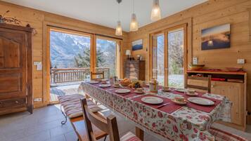 Un intérieur en bois avec une table à manger pour quatre personnes, un buffet en bois et une vue sur les montagnes grâce à de grandes fenêtres.