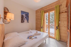 A hotel room with a bed, a wall-mounted lamp, a framed picture, and a window with curtains. - Chalet Les Airelles Mont-Blanc View, Chamonix, France (Chamonix)