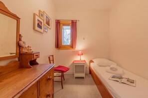 A small, cozy bedroom with a wooden dresser, a chair, a bedside table with a lamp, and a single bed. - Chalet Les Airelles Mont-Blanc View, Chamonix, France (Chamonix)