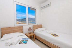 Habitación de hotel con dos camas, una ventana con vista a la ciudad, un equipo de aire acondicionado y una revista sobre la cama.