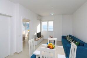 A modern living room with a dining table, a blue sofa, and a TV. - Richard Sea View Apartment, Vlore, Albania (Vlore)