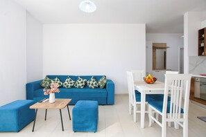 Ein modernes Wohnzimmer mit einem blauen Sofa, einem Holztisch und einem Essbereich mit weißen Stühlen.