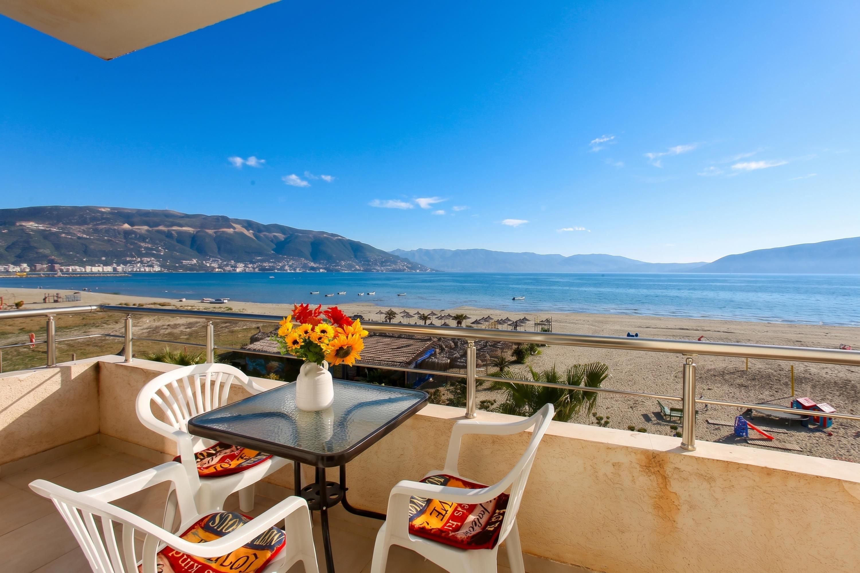 Un balcon avec une table et des chaises, donnant sur une plage et la mer.