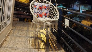 Un balcon doté d’une chaise suspendue, d’une rambarde en métal et d’un sol carrelé.