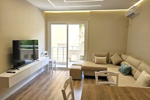 Ein modernes Wohnzimmer mit Flachbildfernseher, einer Couch, einem Esstisch und einem Balkon mit Geländer.