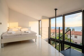 Una camera da letto moderna con un letto, ampie finestre e vista sul mare.