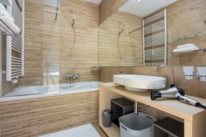 A modern bathroom with a bathtub, a large mirror, a sink, and a hairdryer on the counter.