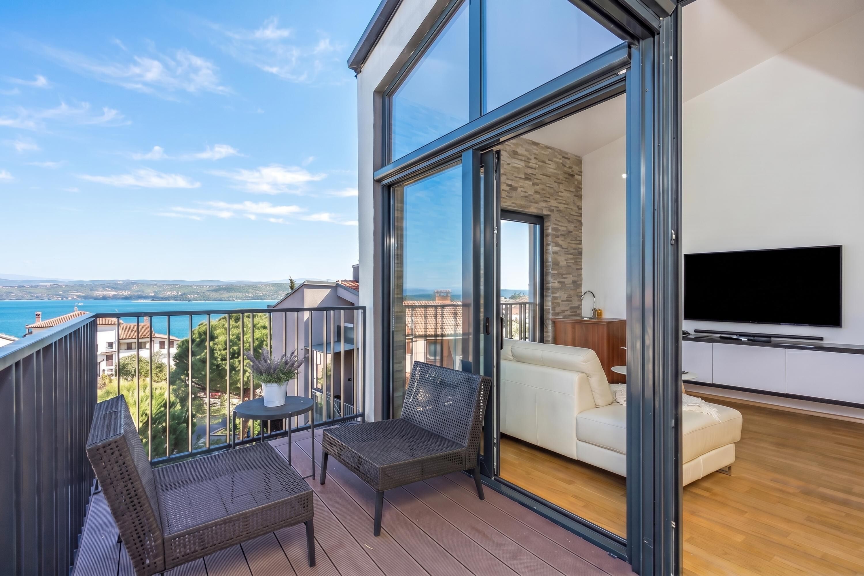 A balcony with wicker furniture, a TV, and a view of the sea.